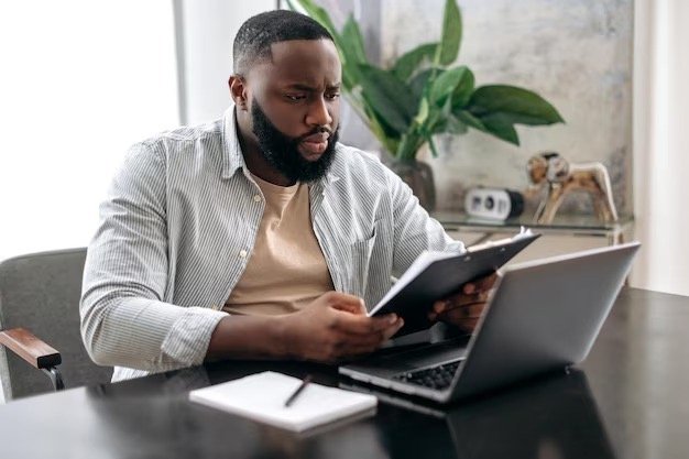 man-reviewing-documents-while-working-on-laptop